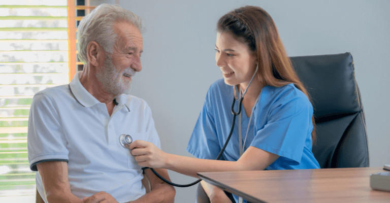 Healthcare professional in blue scrubs using a stethoscope to listen to the chest of an elderly patient, representing Health and Social Care services.