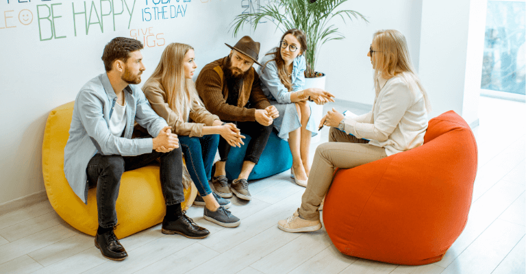 Counselling Skills Training session with a group of people sitting on colorful bean bags, discussing and engaging in conversation in a bright, modern room with motivational quotes on the wall.